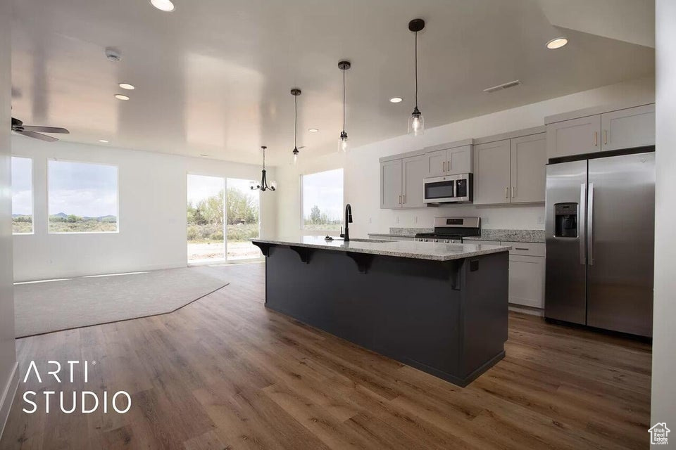 Kitchen with appliances with stainless steel finishes, a breakfast bar area, dark wood-style floors, light stone counters, and a kitchen island with sink
