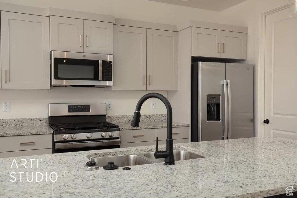 Kitchen with stainless steel appliances, a sink, light stone counters, and white cabinets