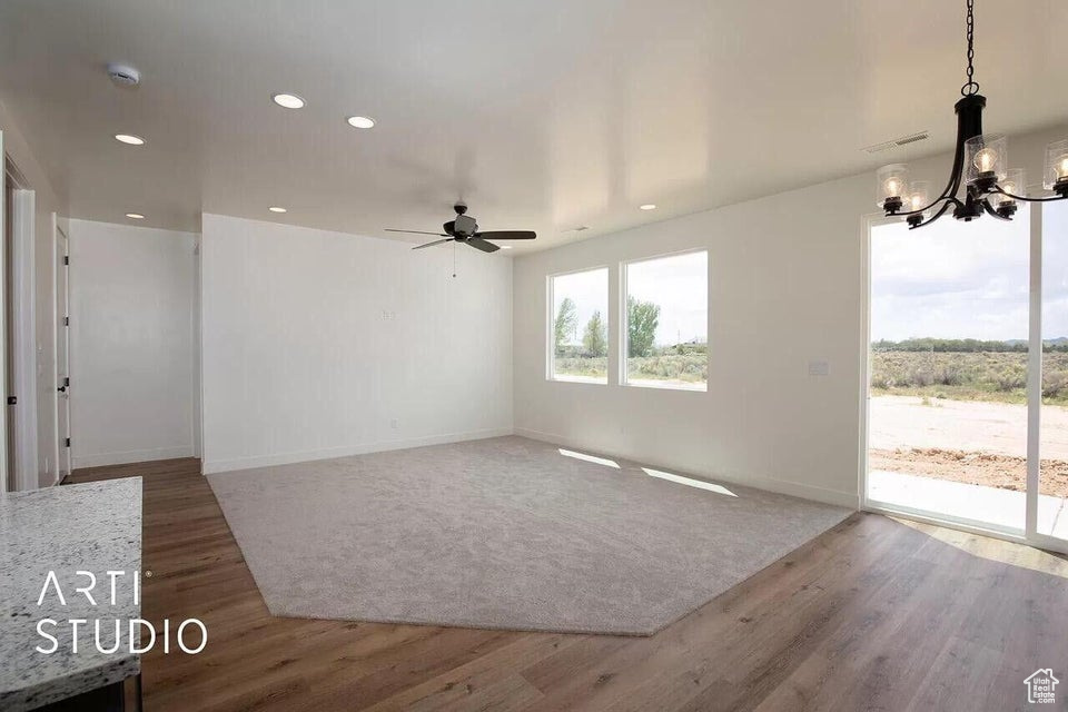 Unfurnished living room with a chandelier, ceiling fan, wood finished floors, recessed lighting, and baseboards