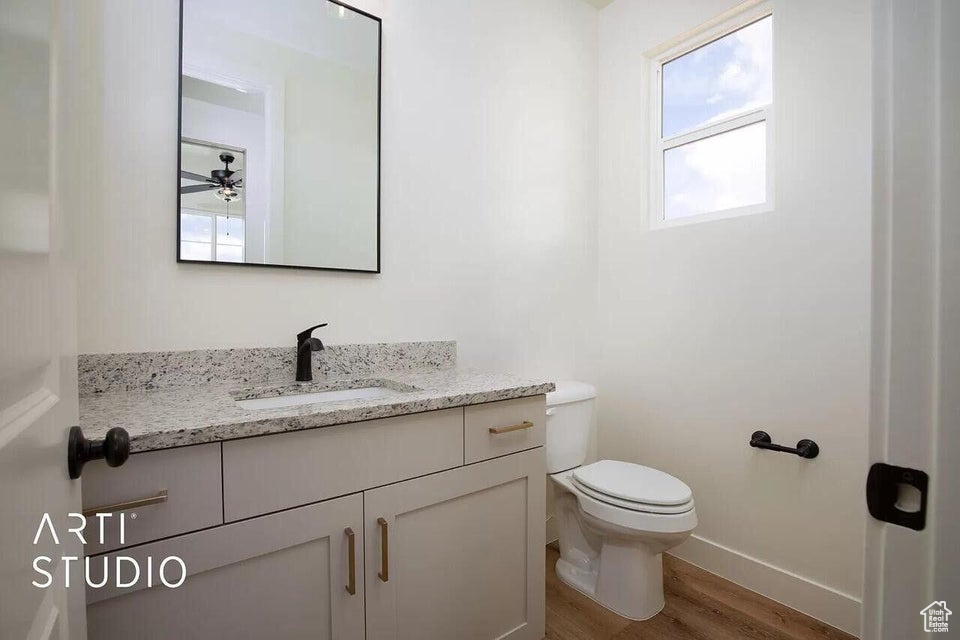 Bathroom with wood finished floors, toilet, vanity, baseboards, and a ceiling fan