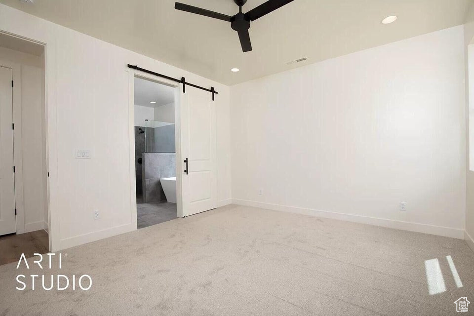 Unfurnished bedroom featuring carpet floors, a barn door, baseboards, recessed lighting, and ensuite bath