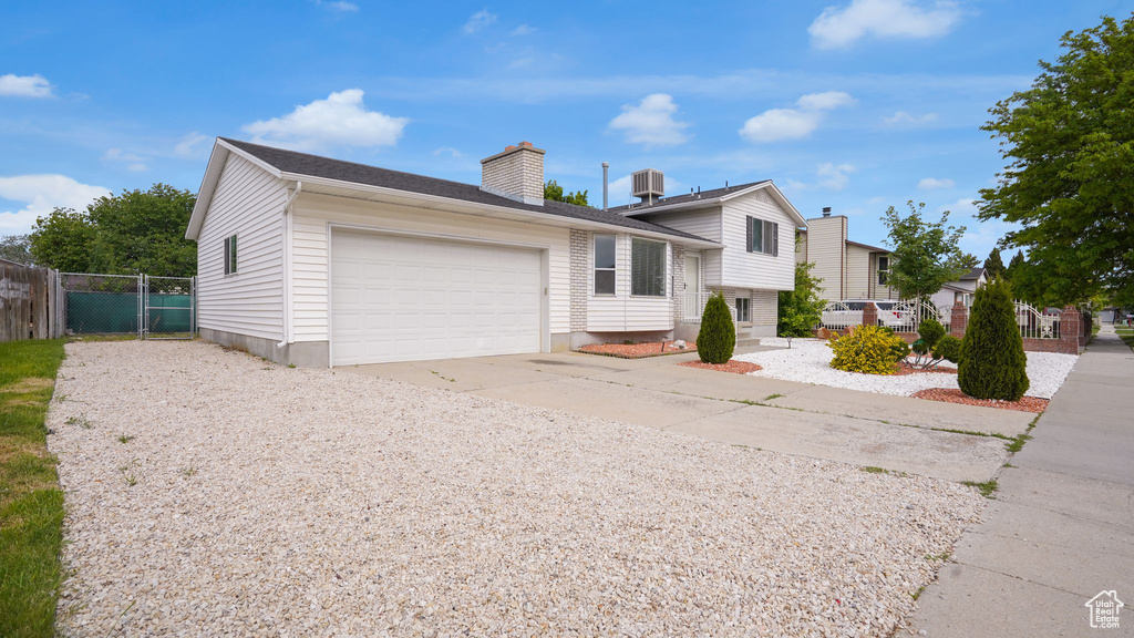 Tri-level home with concrete driveway, a garage, a chimney, and central AC