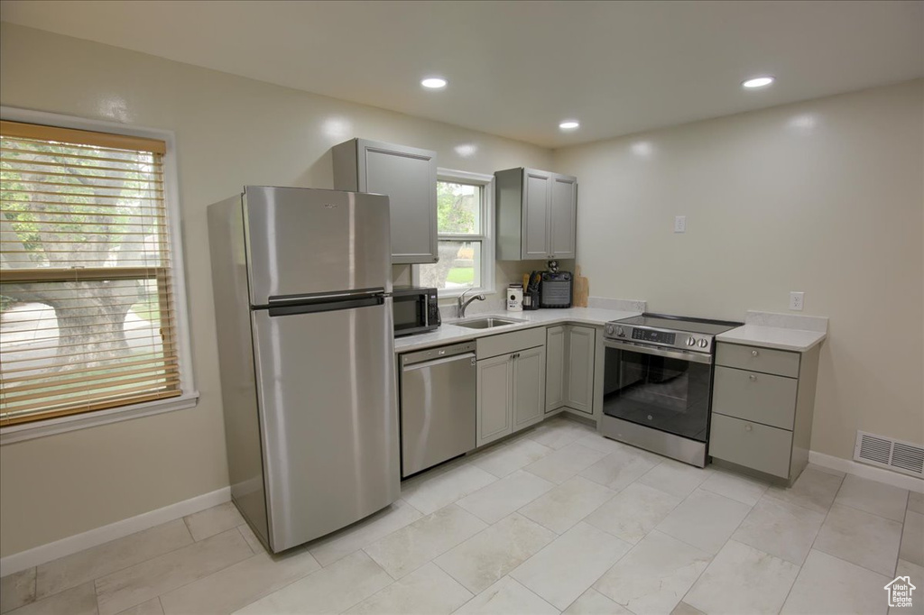 Kitchen with appliances with stainless steel finishes, gray cabinetry, light countertops, baseboards, and recessed lighting