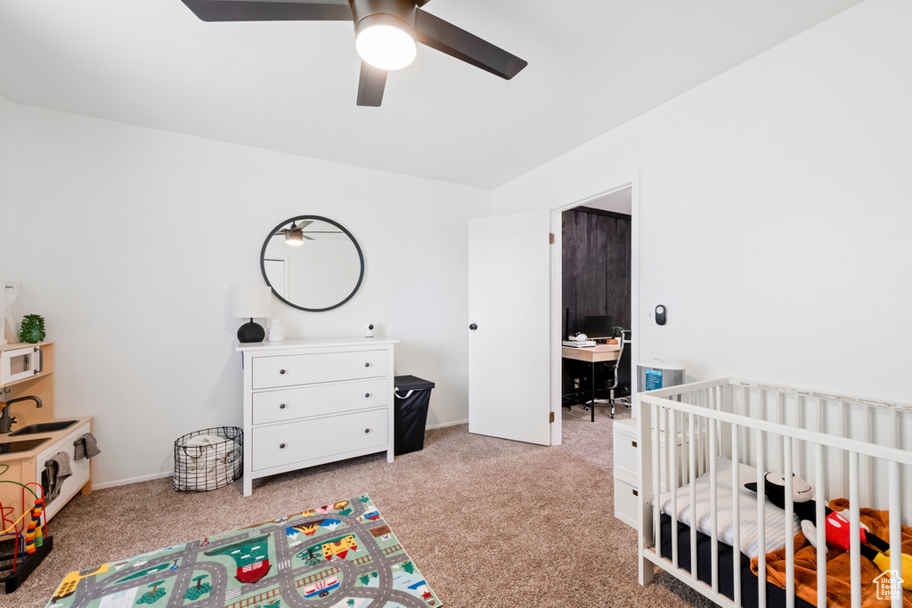 Carpeted bedroom featuring a nursery area, a ceiling fan, and a desk