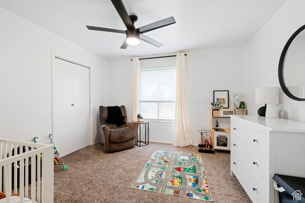 Bedroom featuring light colored carpet, a crib, ceiling fan, and a closet