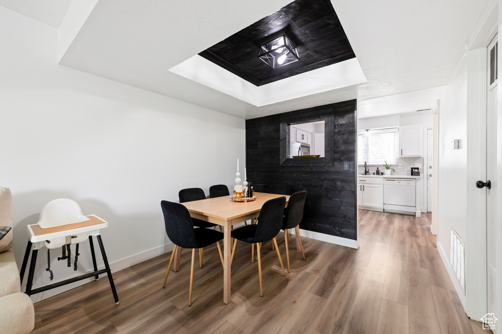 Dining room featuring light wood-style flooring, a raised ceiling, and baseboards