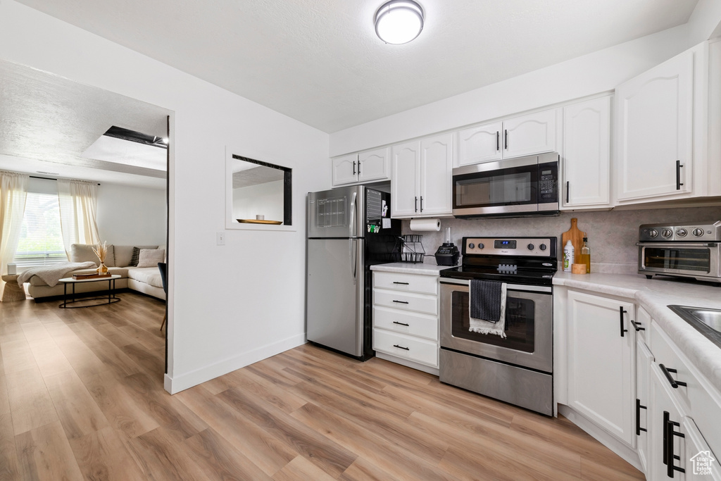 Kitchen with appliances with stainless steel finishes, light countertops, backsplash, and white cabinetry