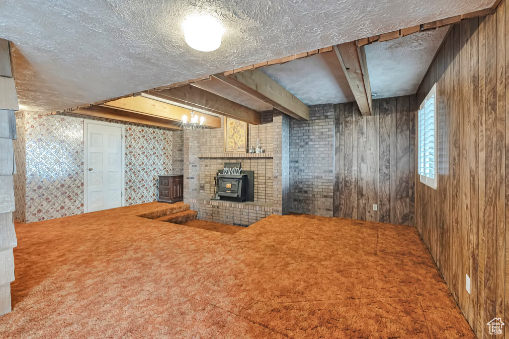 Unfurnished living room with a wood stove, a textured ceiling, wooden walls, and carpet