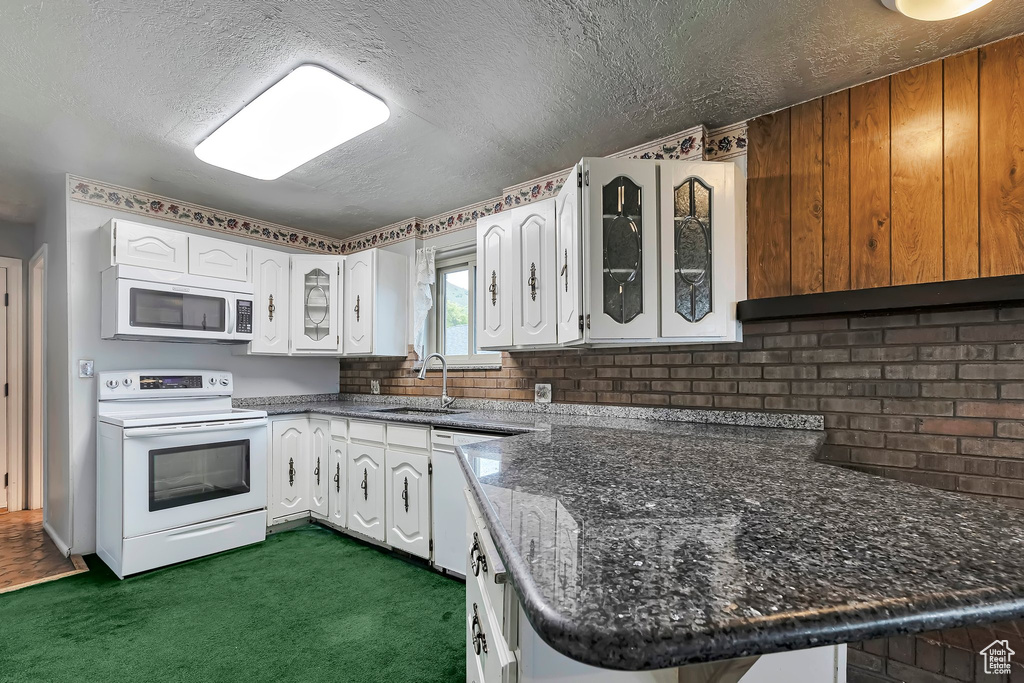 Kitchen with white appliances, a sink, a textured ceiling, dark carpet, and glass insert cabinets