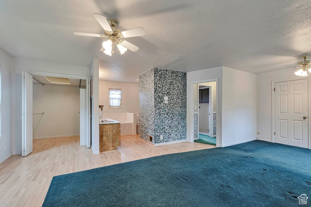 Unfurnished living room with ceiling fan, light wood finished floors, baseboards, and a textured ceiling