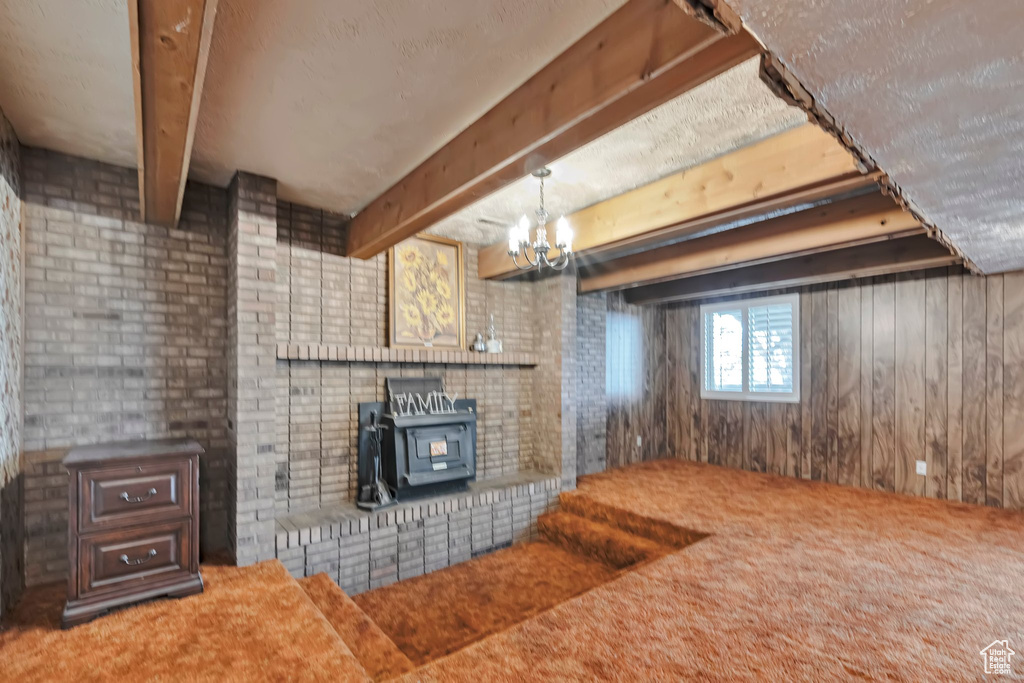 Unfurnished living room with beam ceiling, carpet floors, a wood stove, wooden walls, and a chandelier