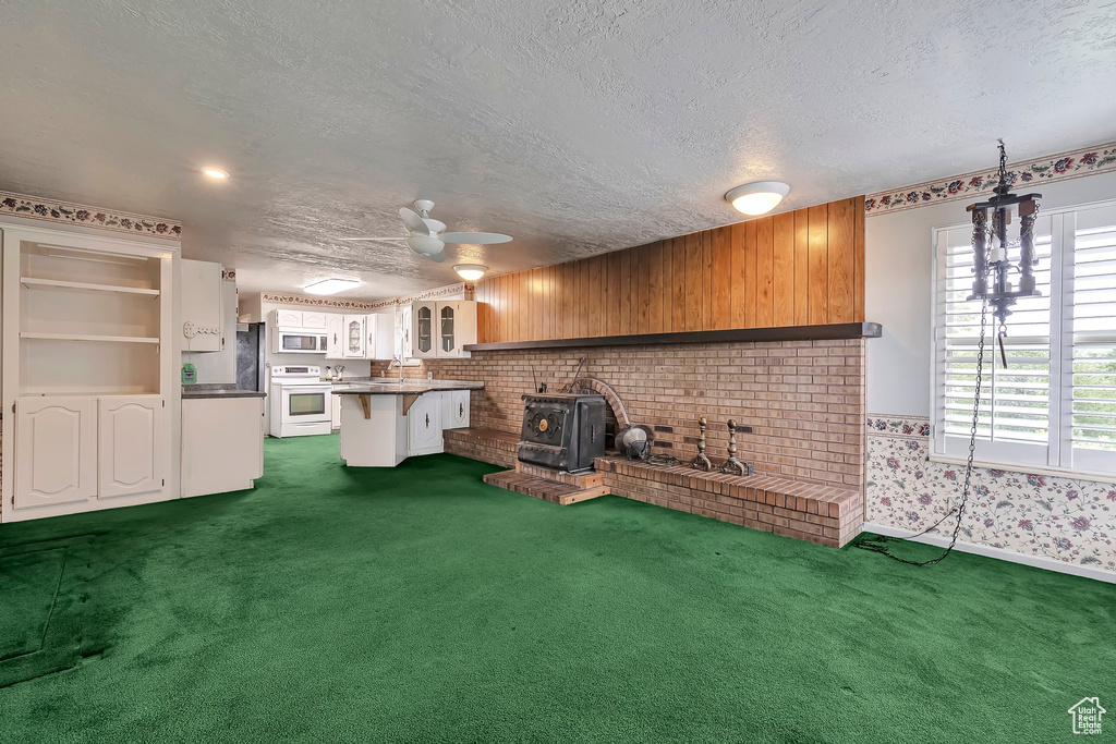 Kitchen featuring white appliances, dark carpet, a kitchen breakfast bar, a textured ceiling, and a wood stove