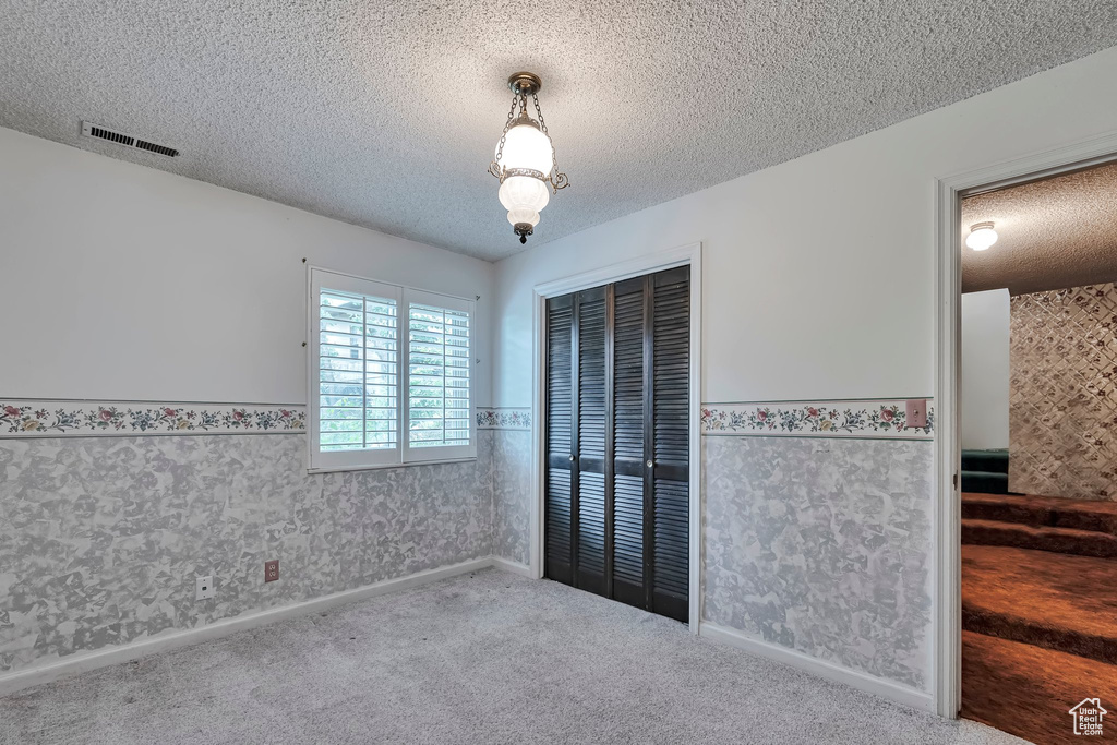 Unfurnished bedroom featuring wainscoting, a textured ceiling, carpet flooring, a closet, and wallpapered walls