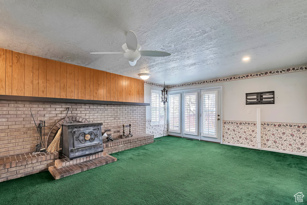 Unfurnished living room with a wood stove, a ceiling fan, a textured ceiling, and carpet