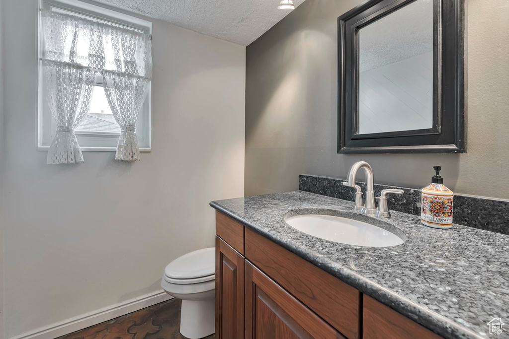 Bathroom with toilet, a textured ceiling, baseboards, and vanity