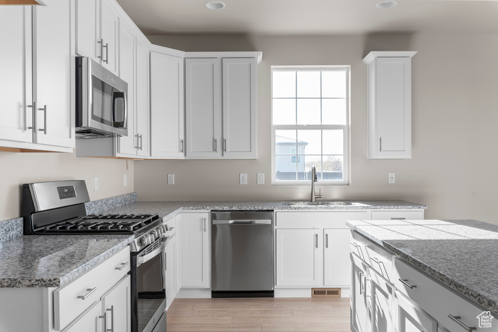 Kitchen featuring appliances with stainless steel finishes, a sink, white cabinets, light wood finished floors, and recessed lighting