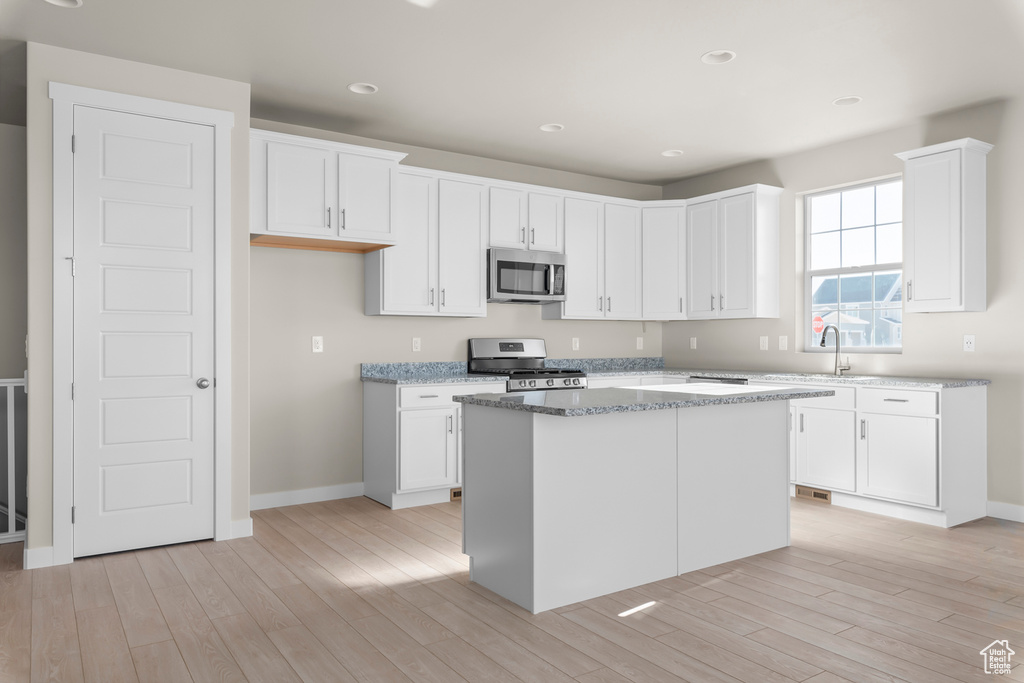 Kitchen featuring stainless steel appliances, light wood finished floors, white cabinetry, baseboards, and recessed lighting