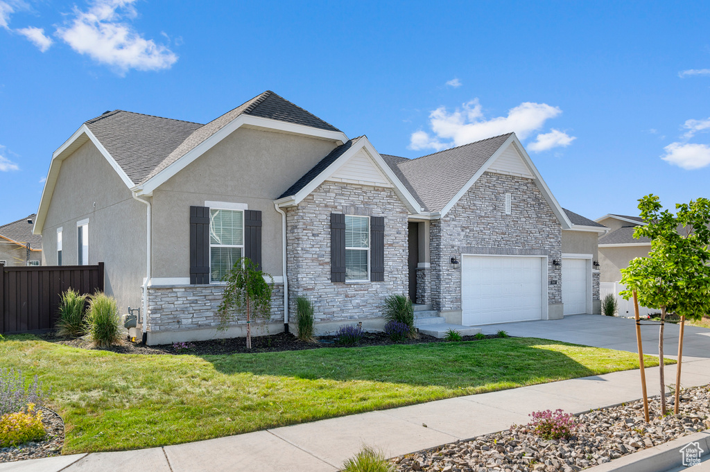 View of front facade with stone siding, an attached garage, driveway, and stucco siding