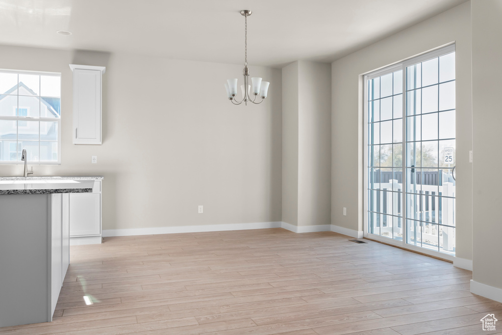 Unfurnished dining area with a chandelier, light wood-style floors, and healthy amount of natural light