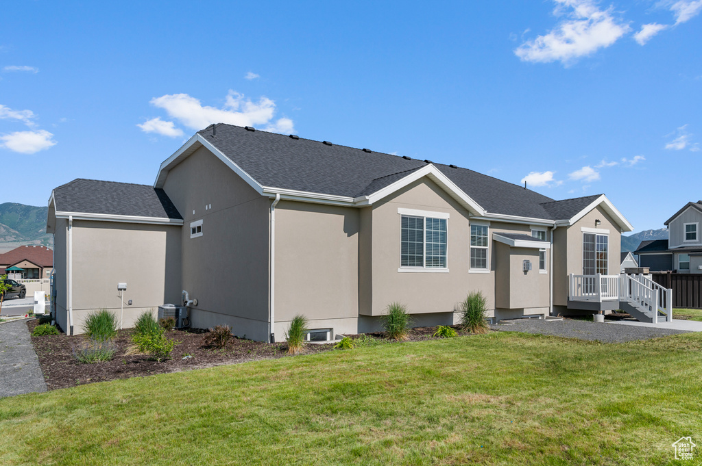 Rear view of property featuring a wooden deck, a lawn, stucco siding, and a shingled roof