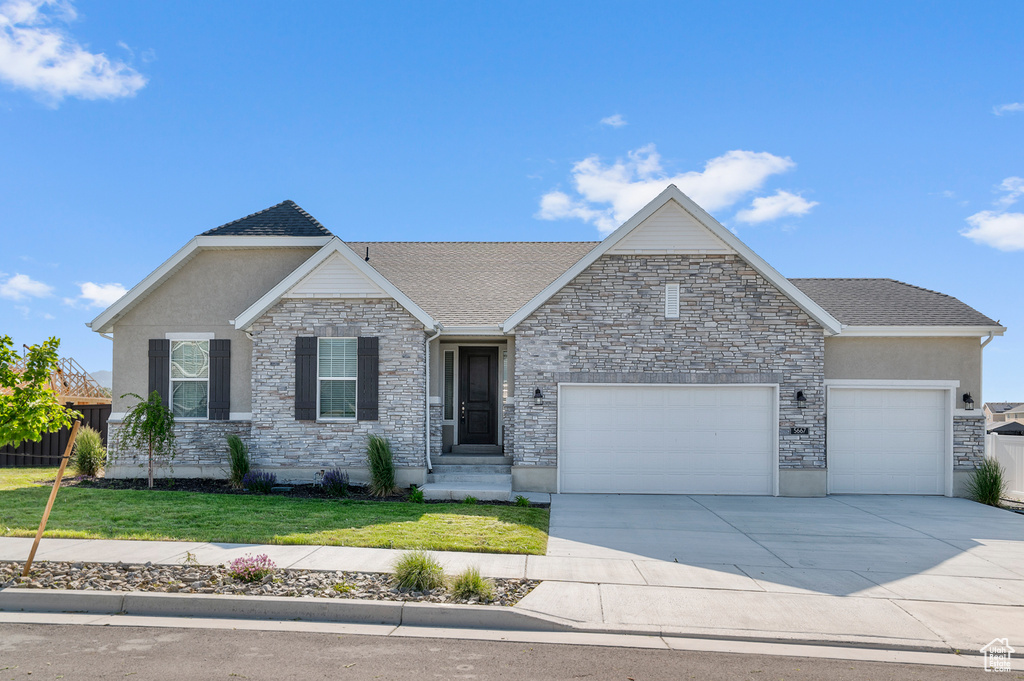 View of front of home featuring a garage, a front lawn, driveway, and stone siding