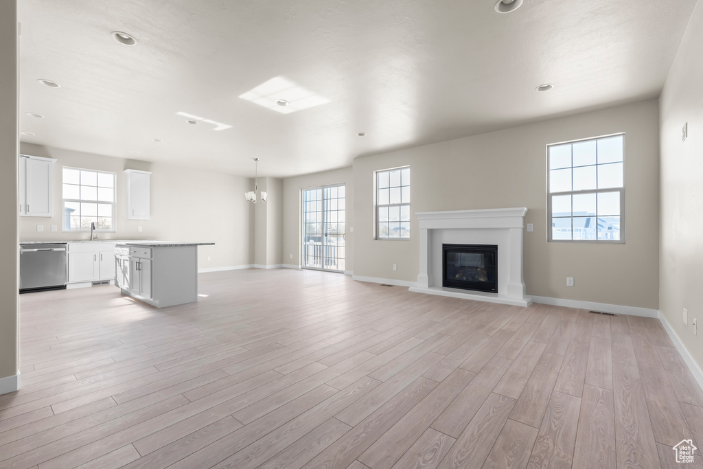 Unfurnished living room with a chandelier, light wood-style flooring, baseboards, and a glass covered fireplace