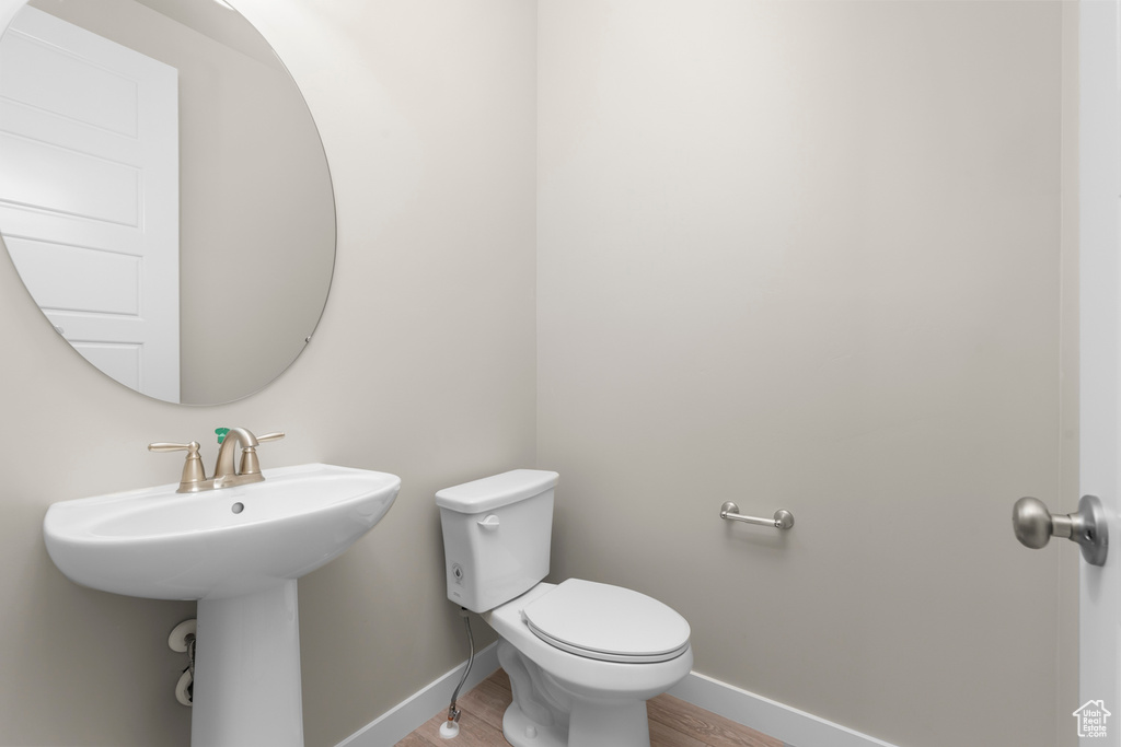 Bathroom featuring baseboards, toilet, wood finished floors, and a sink