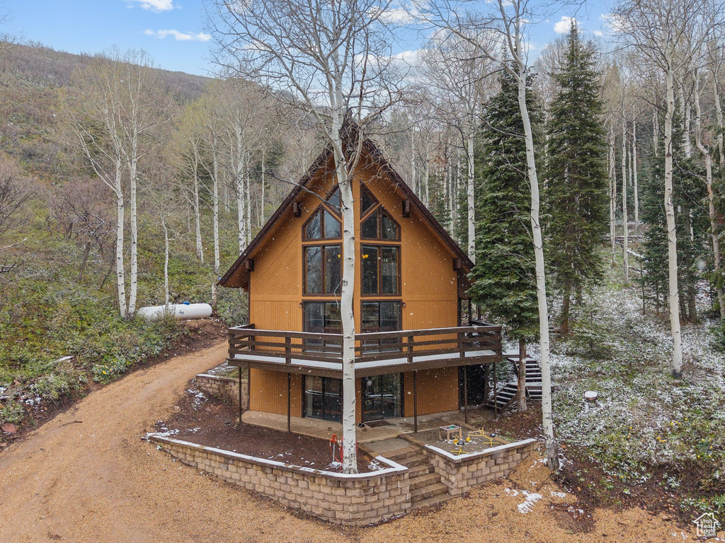 View of front of property with a wooden deck, a wooded view, and dirt driveway