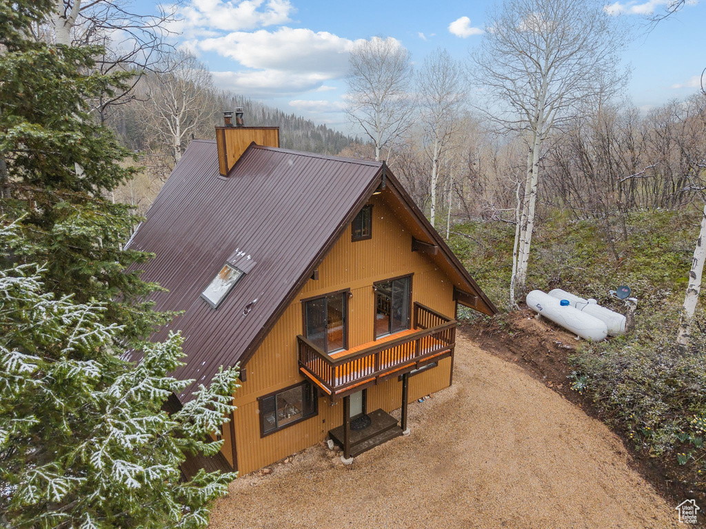 View of side of home featuring a chimney, a wooden deck, driveway, and a view of trees