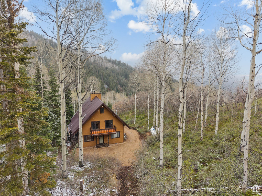View of front of home with a view of trees, stucco siding, and a chimney