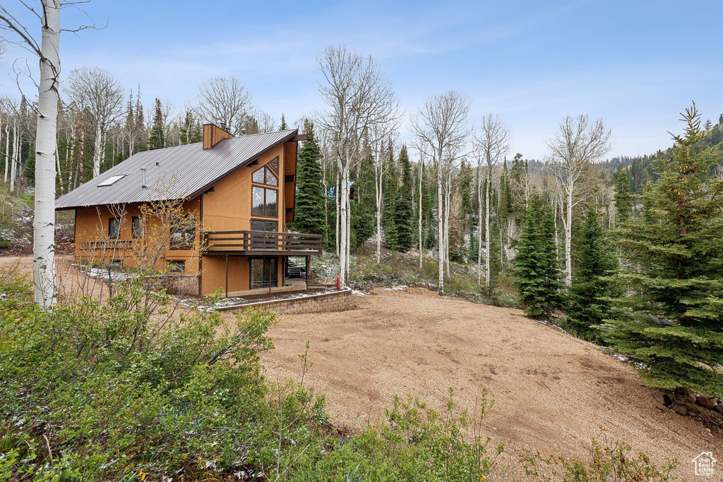 Rear view of house featuring a deck, metal roof, dirt driveway, and a wooded view