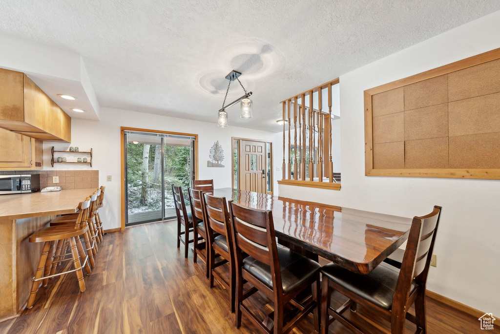Dining room featuring dark wood-type flooring, baseboards, a textured ceiling, and recessed lighting