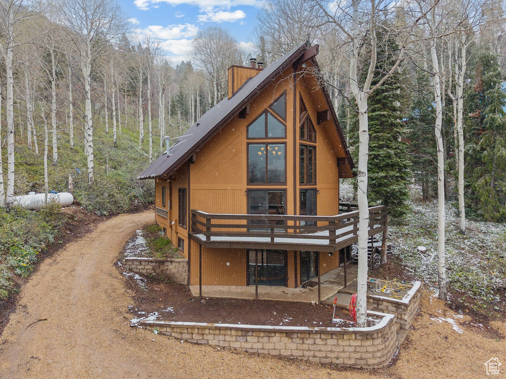 Rear view of property featuring a deck, a chimney, a wooded view, driveway, and a patio