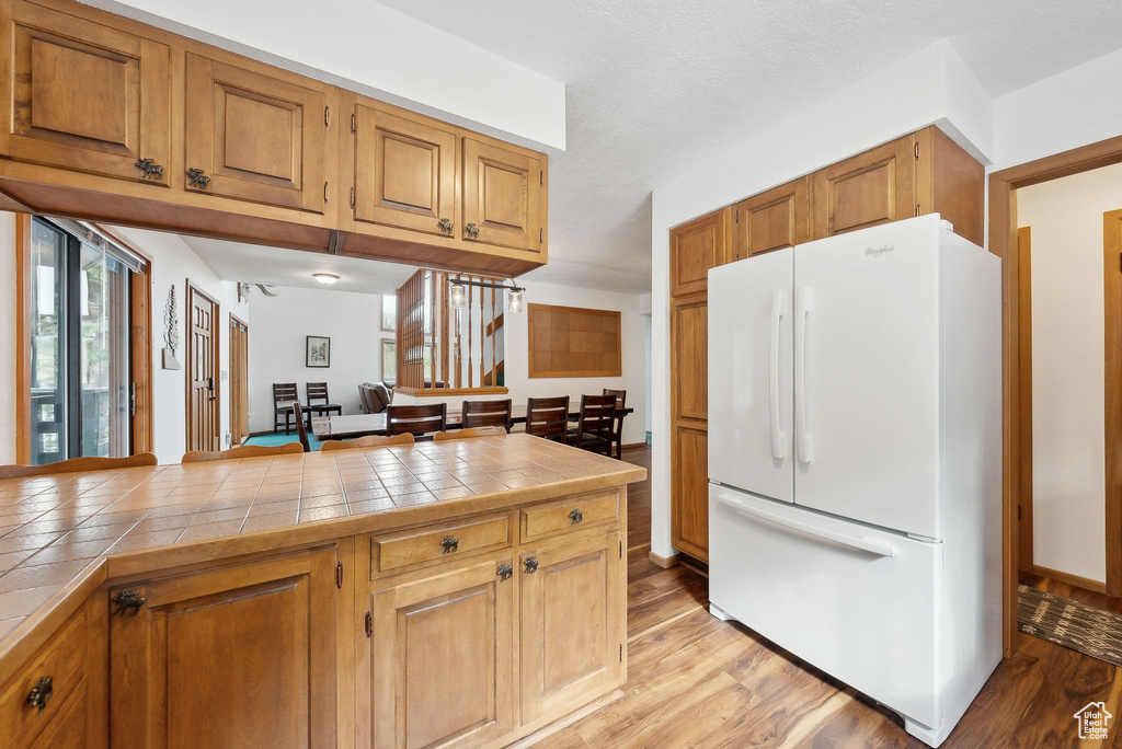 Kitchen with freestanding refrigerator, tile counters, light wood-style floors, and brown cabinets