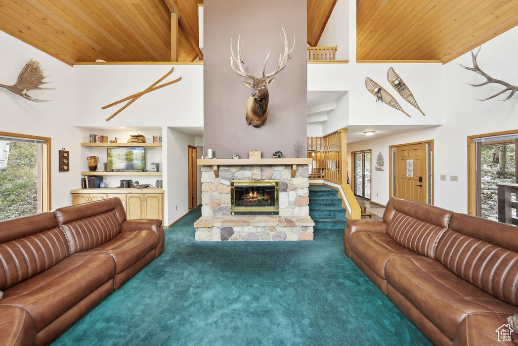 Carpeted living room with wooden ceiling, a stone fireplace, a towering ceiling, stairs, and built in features