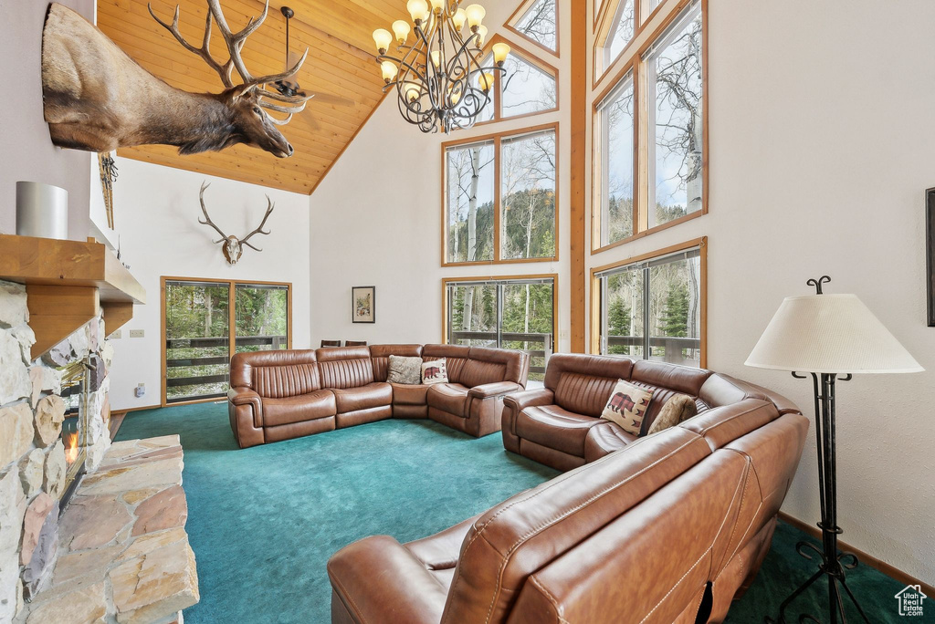 Living area with high vaulted ceiling, carpet flooring, a chandelier, a stone fireplace, and baseboards
