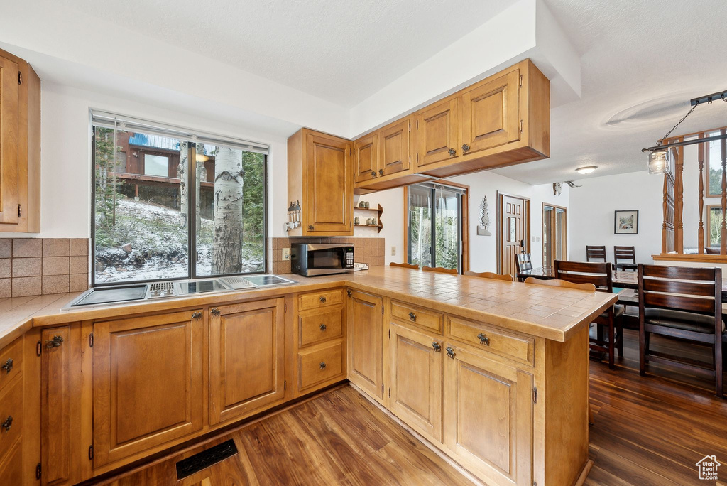 Kitchen featuring stainless steel microwave, a peninsula, backsplash, tile countertops, and dark wood-type flooring