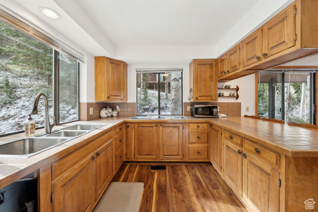 Kitchen featuring stainless steel microwave, a sink, tile counters, dark wood-style floors, and recessed lighting