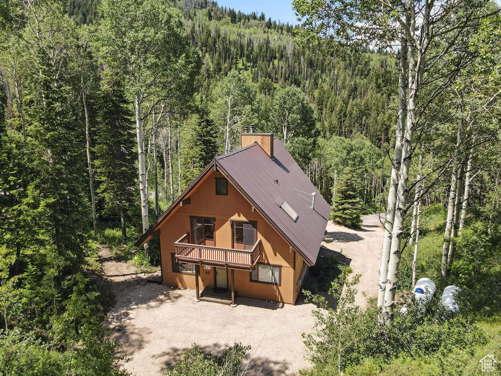 View of front of home with a forest view, a metal roof, driveway, and a deck