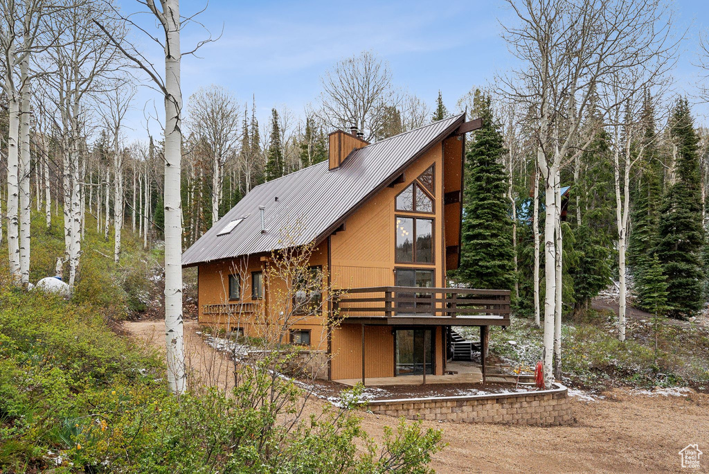 Back of house featuring metal roof, a chimney, a deck, and stucco siding