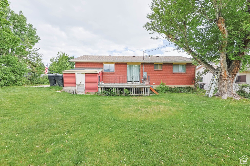 Back of house with brick siding, a yard, and a deck