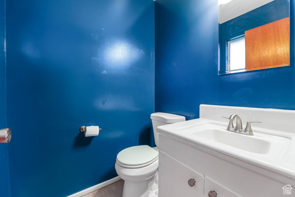 Half bath with toilet, wood finished floors, and vanity