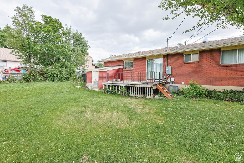 Back of house featuring a yard, a wooden deck, and brick siding
