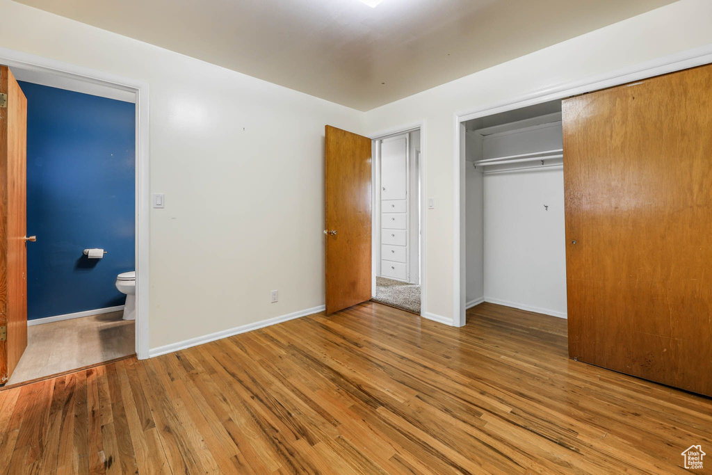 Unfurnished bedroom featuring wood finished floors, a closet, baseboards, and ensuite bathroom