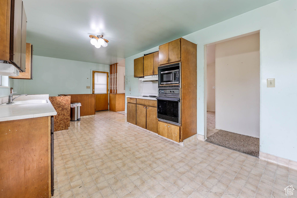 Kitchen featuring black oven, a sink, built in microwave, and light flooring