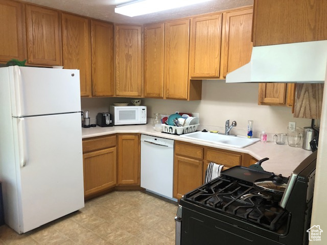 Kitchen with white appliances, a sink, light countertops, and brown cabinetry