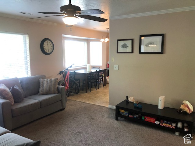 Living area featuring carpet flooring, crown molding, a ceiling fan, and a chandelier