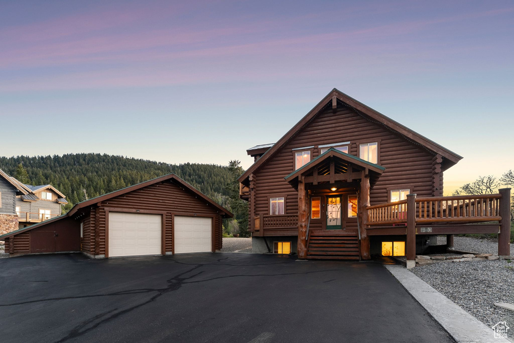 Log home with log siding, a detached garage, an outdoor structure, and a wooded view