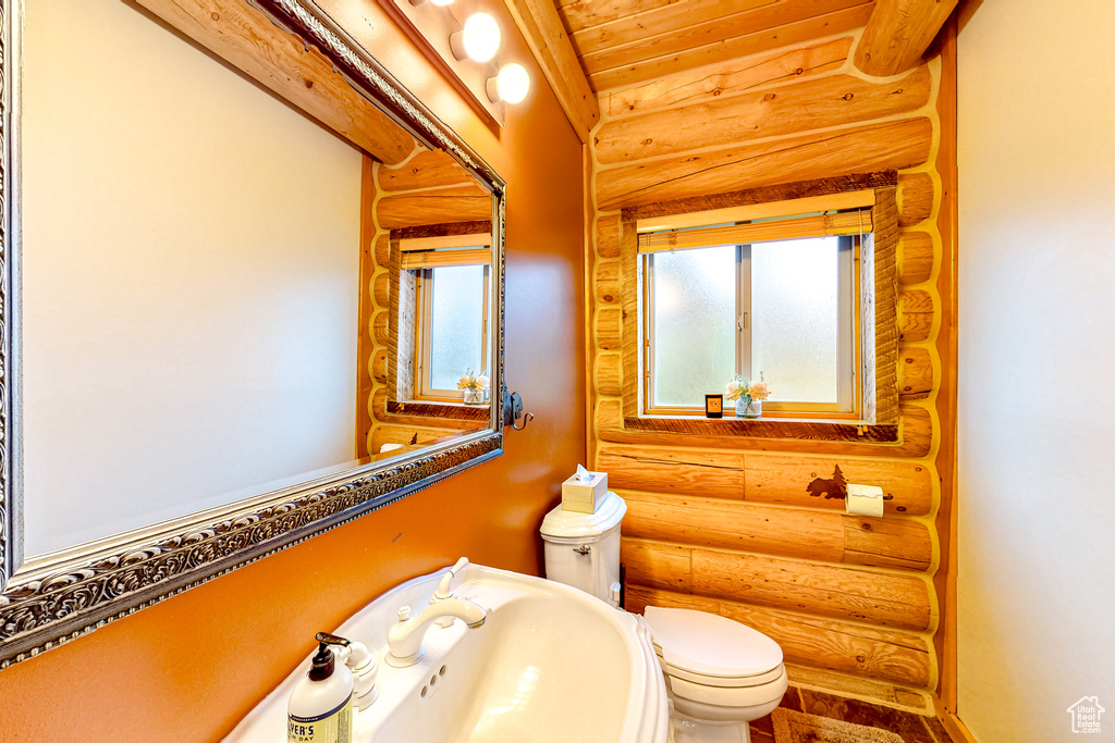 Bathroom featuring rustic walls, toilet, wood ceiling, and a sink