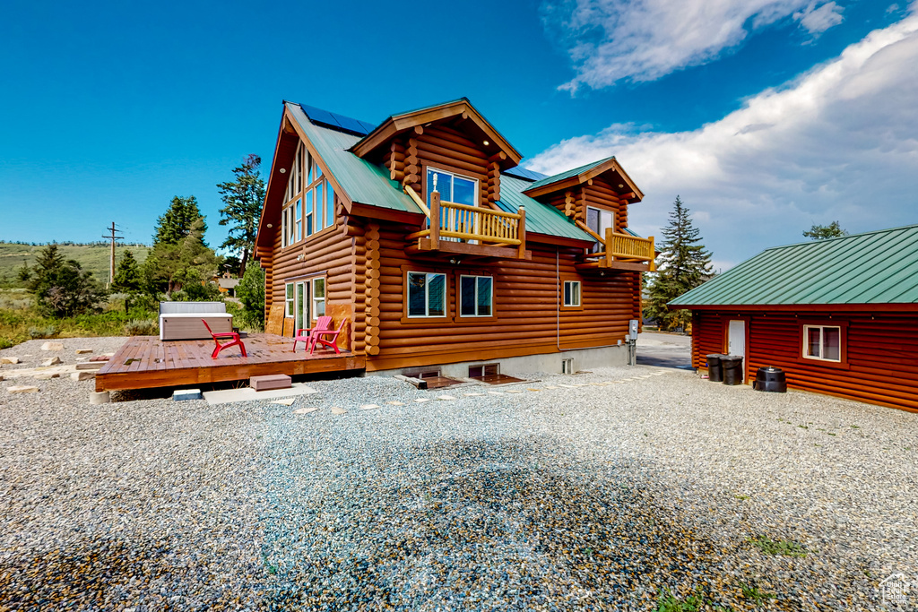 Rear view of house featuring log exterior, metal roof, a deck, a balcony, and roof mounted solar panels